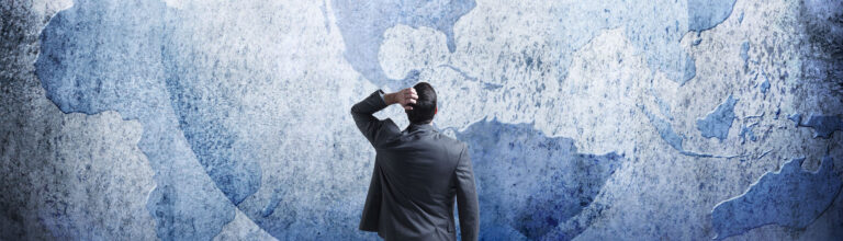 Businessman Stands And Looks Up At Three Interlocking Globes On Wall
